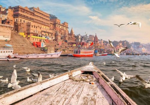 Historic,Varanasi,City,Architecture,With,Ganges,River,Ghat,At,Sunset Historic Varanasi city architecture with Ganges river ghat at sunset with view of migratory birds